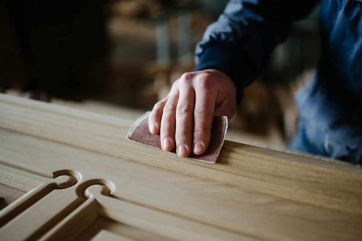 Hand plane, sandpaper, small can of primer and paintbrush laid out on a drop cloth next to a removed door