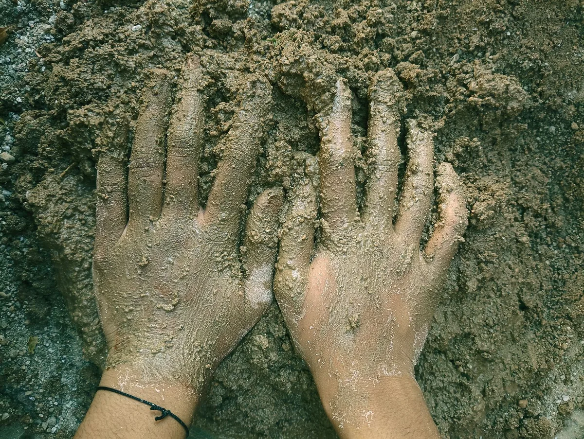A pair of hands covered in muddy clay, showcasing a natural earthy texture.