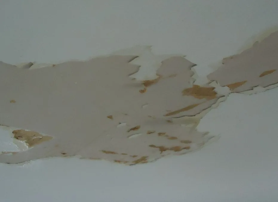 Hand pressing against water-damaged drywall behind a bathroom tile, showing soft crumbling material